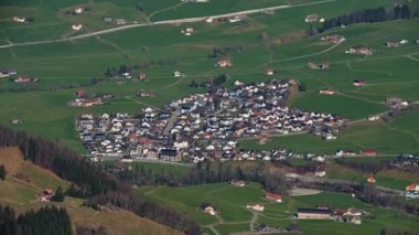 Küçük bir kasaba, sayısız ev ve yeşil tarlalarla dağlarda yuva kurar. Yollar binaları birbirine bağlıyor ve açık alanlar açık mavi gökyüzünün altında.