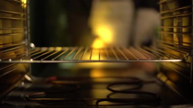 Bir şefin sıcak fırının içine kek hamuru koyduğu yakın plan. Karışım, yumuşak altın ışık altında yükselir ve ısınır sıcak bir atmosfer yaratır. Görüntüler tatlıya hazırlanmayı temsil ediyor