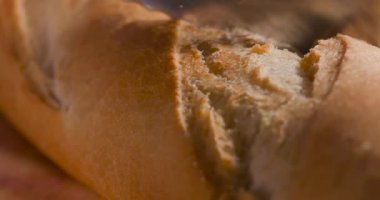 Bir fırıncı yoğun bir mutfakta taze ekmek hazırlar. Kabuğu kesilmiş, yumuşak ve sıcak kırıntılar ortaya çıkıyor. Müşteriler siparişlerini beklerken koku havayı dolduruyor..