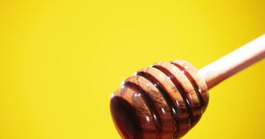 Tahta bir balıkçı balını yüzeye damlatırken tutar. Sarı arkaplan, balın koyu altın rengiyle çelişiyor, dokusunu ve parlaklığını vurguluyor..