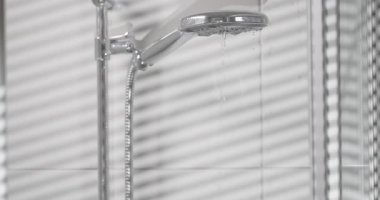 Banyodaki duş başlığından su akar. Işık, duvarlarda desenler oluşturur ve duş camından zemin oluşturur. Mekan parlak ve fayanslarla modern..