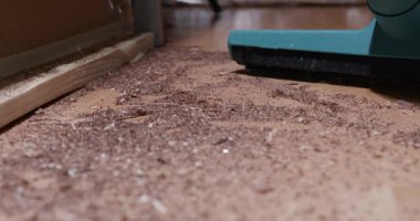 Bir insan ahşap zeminden talaş ve toz çıkarmak için elektrikli süpürge kullanır. Temizlik öğleden sonra bir atölyede yapılır..