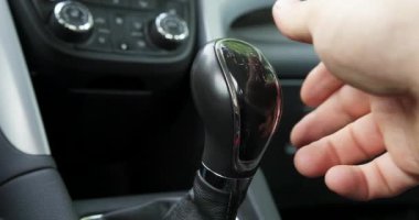 Bir el arabanın vites koluna uzanır. Sürücü gün boyunca işlek şehir caddelerinde gezinirken vites değiştirmeye hazırlanıyor..