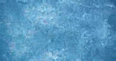 Su, berrak bir havuzda güneş ışığıyla yavaşça akar ve yansımalar yaratır. Küçük dalgalar hareket ettikçe yüzey parlıyor. Ortam aydınlık ve sıcak..