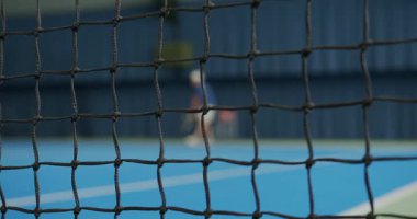 Oyuncular kapalı tenis kortunda antrenman yaparlar. Ağ hareket ettikçe odak noktasında, tesiste salıncaklar ve atışlar üzerinde çalışıyorlar..