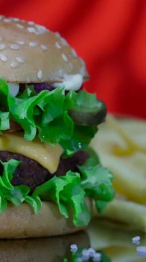 Bir hamburger marul, erimiş peynir ve turşu katmanları ile sergilenir. Patates kızartması, hamburgerin yanına ahşap bir yüzeye yerleştirilir. Parlak renkler lezzetli bir görünüm yaratır..