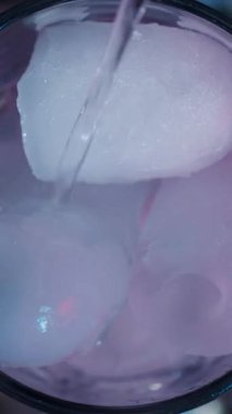 Bir insan, yukarıdan gelen su serin ve ferahlatıcı elementlerin karışımını oluştururken bir kabın içine buz küpleri ekler. Süreç ve içki hazırlığı üzerinde duruluyor..