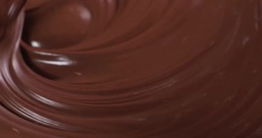 Bir insan spatulayla çikolatayı bir kasede birleştirir. Çikolata zengin ve kalın. Karışım mutfak tezgahında oluyor, parlak bir karışım oluşturuyor..