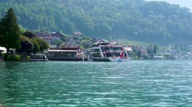 İnsanlar köyün ve tepelerin tadını çıkarırken bir gölde tekne turu yapıyorlar. Güneş parlıyor ve teknenin etrafında berrak sular var..