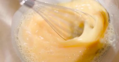 Bir insan açık bir kasede yumurta karıştırmak için çırpıcı kullanır. Yumurtalar pürüzsüz olana kadar birleştirilir. Aksiyon bir mutfak ortamında gerçekleşir, yemek hazırlamak için..