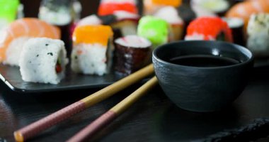 Taze suşi renkli malzemelerle siyah bir tabakta düzenlenir. Soya sosu küçük bir kasede. Çubuklar yakına yerleştirildi, kullanıma hazır..
