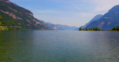Yüksek dağlar ve yemyeşil alanlar tarafından çerçevelenmiş temiz suyla geniş bir göl. İsviçre 'de güneşli bir günde küçük bir tekne gölde yavaşça hareket eder..