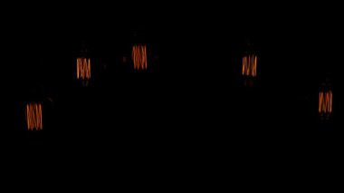 Loş bir alanda tavandan farklı ampuller sarkıyor. Sıcak parıltı bölgeyi aydınlatarak rahatlama ve toplanma için rahat bir ortam sağlıyor..