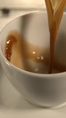 Süper yavaş çekimde koyu espresso beyaz fincana dökülüyor, krema oluşumuna yakın çekim, sıcak altın tonlar, yumuşak