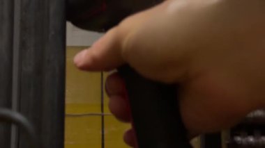 Bir işçi bir depodaki ekipmanları ayarlamaya odaklanırken bir aleti kavrıyor. Etkinlik yoğun bir öğleden sonra vardiyası sırasında gerçekleşir. Makinelerin arka plan sesleri duyulabilir..