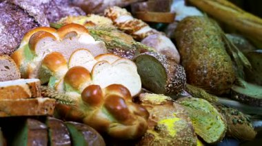 Marketteki bir masada çeşitli ekmekler düzenlenir. Her ekmeğin kendi şekli ve rengi var. İnsanlar farklı ekmek türlerini seçerken ve alırken görülebilir..