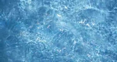 Dalgalar berrak mavi suyla dolu bir yüzme havuzunun yüzeyinde hareket eder. Güneş ışığı sudan yansıyarak öğleden sonra boyunca değişen desenler yaratır..