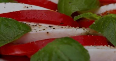 Doğranmış domates ve mozzarella kesme tahtasında taze fesleğen yapraklarıyla kaplıdır. Zeytinyağı ve baharatlar lezzeti arttırmak için eklenir..