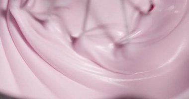Bir insan, el mikseriyle bir kasede pembe krema karıştırıyor. Parlak renk ve kremsi doku mutfakta eğlenceli bir atmosfer yaratıyor. Bu güneşli bir öğleden sonra olur..