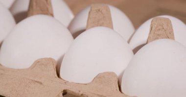 Bir grup beyaz yumurta bir karton içinde düzenlenir. Ayarlar, yumuşak ışıklı bir marketin geldiğini gösteriyor. Müşteriler etrafta dolaşıp ürünlere bakarlar..