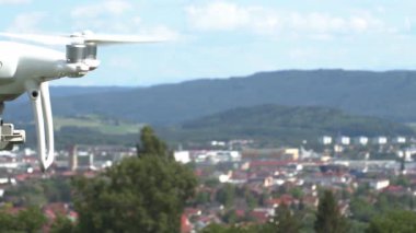 Bir dron şehrin üzerinde uçar ve güneşli bir günde binaları, yeşil ağaçları ve uzak tepeleri net bir şekilde görür. İnsanlar aşağıdaki açık havanın tadını çıkarırken görülebilir..
