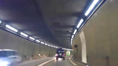 Gece bir araba tünelden geçiyor. Parlak ışıklar duvarları çiziyor ve yeşil trafik ışıkları yolu gösteriyor. Araçlar hareket ettikçe atmosfer canlanıyor..