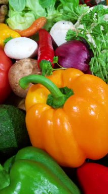 Parlak turuncu çan biberi önplanında karışık sebzeler, parlak kabuklar, yapraklı yeşiller ve mantarlar var.,