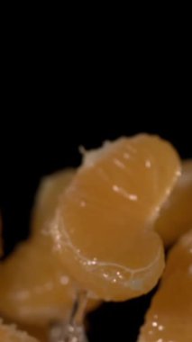 Süper yavaş çekimde mandalina dilimleri yavaş çekimde siyah zemine çarpıyor, su boncukları ve çarpma