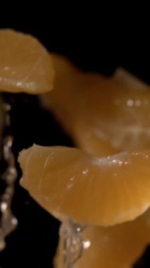 Su damlacıkları, parlak dokular ve siyah renklerle ağır çekimde yükselen süper yavaş mandalina segmentleri