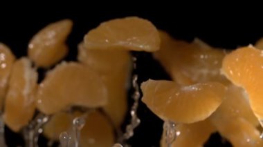 Süper yavaş çekimde mandalina dilimleri siyah arkaplana karşı yükseliyor sulu narenciye segmentlerinin makro yakın çekim makrosu