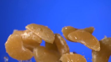 Süper yavaş çekim mandalina segmentleri yavaş çekimde canlı mavi arkaplan boyunca yayılıyor, sıçrıyor