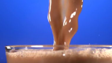 Süper yavaş çekim kalın kakao akıntısı cama dökülüyor, parlak mavi arkaplan, parlak sıvı kurdele,