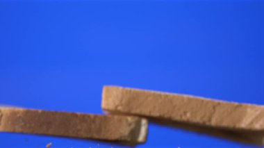 Süper yavaş çekimde kızarmış ekmek dilimleri mavi arka planda uçuşuyor, kırıntılar aşağıda dağılıyor, yakın plan.