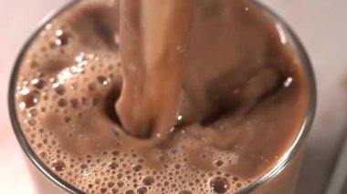 Süper yavaş çekim. Cama dökülen kremalı kakao köpüklü kabarcıklar ve kıvrımlı, zengin kahverengi akıntı oluşturur.,