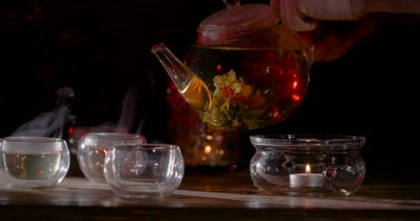 Elle Çiçek açan çayı cam bardaklara dökerek, Buharla tahta masa üstünde yükselerek, Kehribar aşılayarak çiçek açarak,