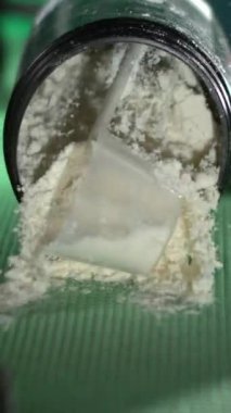 Süper Yavaş Çekim Makro Kapalı Kavanoz Protein Tozu Yeşil Mat 'a dökülüyor, Plastik Kepçeyi Temizle Yarısı Gömülü