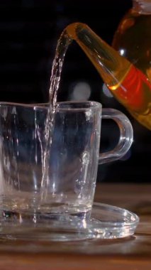 Kehribar çayıyla doldurulmuş cam bardak, temiz çaydanlık, ahşap masa üstüne sabit akarsu dökülmüş, altın rengi.