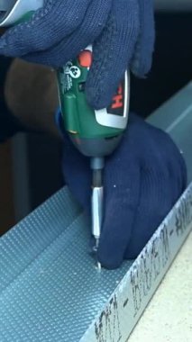 Bir işçi atölyedeki metal levhayı korumak için kablosuz matkap kullanıyor. Malzeme üzerinde çalışırken el aleti kavrıyor. Üretimde montaj aşamasını gösterir.