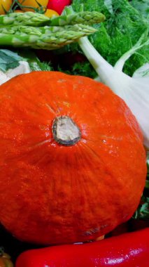 Markette çeşitli meyve ve sebzeler gösteriliyor. Parlak turuncu bir balkabağı da dahil. İnsanlar sonbahar mevsiminde taze ürün için alışveriş yaparlar..