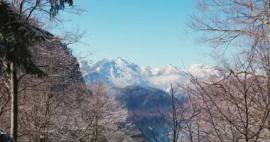 Kameralar dağları ve gölü gösterirken kar zemini ve ağaçları kaplıyor. Güneş açık mavi bir gökyüzünde parlıyor. Bu görüntü Alpler 'de bir kış günü meydana gelir..