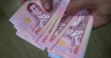 Bangkok 'ta işlek bir pazarda Tayland banknotlarını gösteren eller. Kamera sayıldığı gibi paranın detaylarını yakalar. İnsanlar arka planda ve dükkanda yürürler..