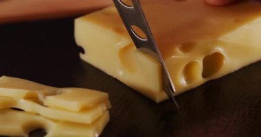 Bir insan mutfakta peynir kesiyor. Peynirin delikleri ve pürüzsüz bir dokusu var. İnce dilimler servis için dikkatlice hazırlanıyor..