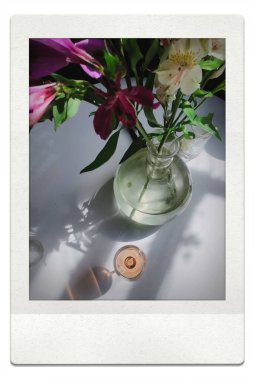 Fotoğraf gibi polaroid, çiçekli vazo ve gül şarabı masanın üzerinde içilir. 