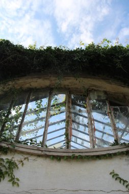 Eski köy evi, terk edilmiş cam pencereli ve bitkili bina. 