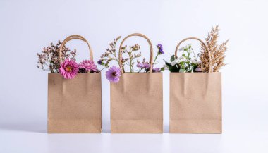 Üç kahverengi çuval, bağlı çiçekler, yapraklar ve kuru otlarla süslenmiş, beyaz arka planda izole edilmiş. 