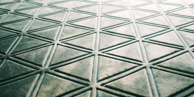 Koyu gri kauçuk bir yüzeyin detaylı bir görüntüsü ve tekrarlanan üçgen şablonu. Dokuma malzemesi spor salonu veya endüstriyel zemin uygulamaları için dayanıklı ve kaymaz bir yüzey sağlar..