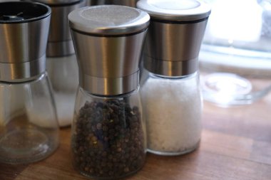 Mutfak masasında ya da tezgahta tuz ve biber öğütücüleri var. Yemek ve yemek pişirme, zarif tasarımı, ahşap ya da metal kaplamaları ve işlevsel kullanımı gösteren çeşnilendirme araçlarının yakın çekimi. Yemek hazırlama, aşçılık yaşam tarzı, mutfak aksesuarları.