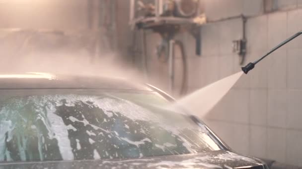 Master πλένει τον αφρό από το μαύρο sedan με ένα σωλήνα με νερό — Αρχείο Βίντεο