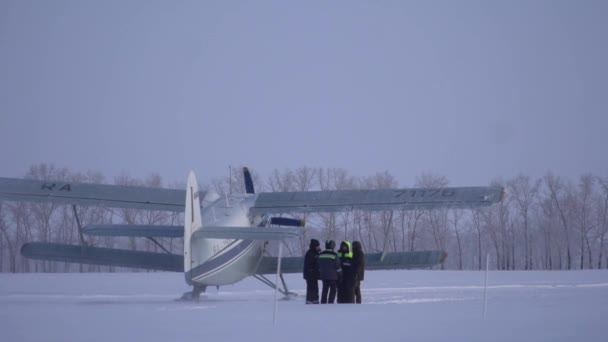 Biplan An2 atterrissant sur neige. Les lames tournent. Ciel bleu, arbres en arrière-plan. — Video