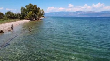 Yunanistan 'da yoğun yeşil bitki örtüsüyle çevrili gizli bir sahil. Sakin turkuaz deniz, yakındaki dağları yansıtarak mükemmel bir Akdeniz manzarası oluşturur..